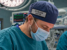 Load image into Gallery viewer, Doctor wearing a blue cap with 'Dr. Wilson' label in an operating room.
