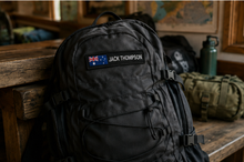 Load image into Gallery viewer, Custom flag patch on a travel backpack in a lodge common room